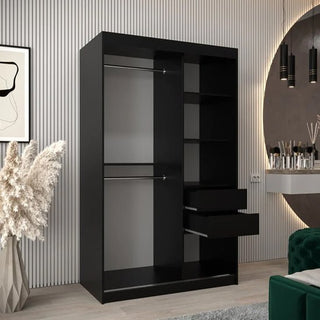 The Tavira Wooden Wardrobe 2 Sliding Doors 120cm in Black features hanging rods, shelves, and two drawers, standing in a modern room with striped walls, abstract art, pampas grass in a vase, and a round mirror.