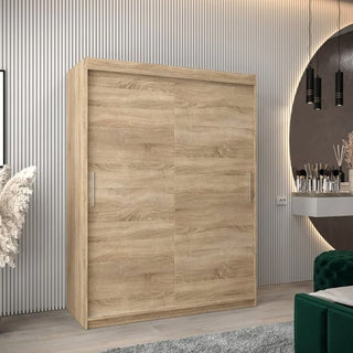 The Tavira Wooden Wardrobe 2 Sliding Doors 150cm in Sonoma Oak stands in a modern room with vertical wall paneling, a round mirror, pendant lights, and a green velvet chair.