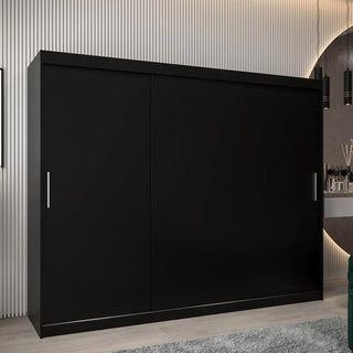 A spacious, modern Tavira Wooden Wardrobe 3 Sliding Doors 250cm in Black with silver handles stands on a light wood floor against a striped wall, next to a round mirror and decorative items.