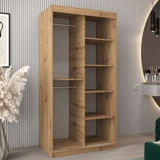 The Vevey I Wooden Wardrobe 2 Sliding Doors 100cm in Artisan Oak stands against a vertically striped wall in a modern room, complemented by dried pampas grass and a wall mirror.