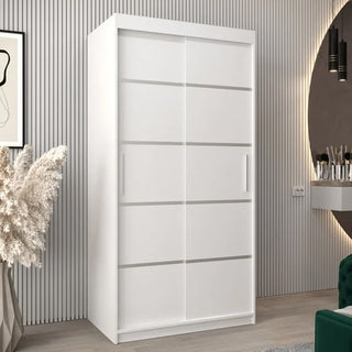 The Vevey I Wooden Wardrobe with 2 white sliding doors (100cm) stands against a wall with vertical grooves, complemented by pampas grass, wall art, a mirror, and a vanity for a modern, minimalistic look.