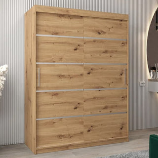 The Vevey I Wooden Wardrobe in artisan oak features two sliding doors and a light natural finish with horizontal silver accents, placed against a grooved wall next to a vanity area with a round mirror.
