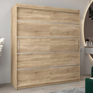 The Vevey I Wooden Wardrobe, 180cm in Sonoma Oak, with two sliding doors and silver horizontal accents, stands against a vertically grooved wall; two silver handles show on the left, and a partial mirror is visible on the right.