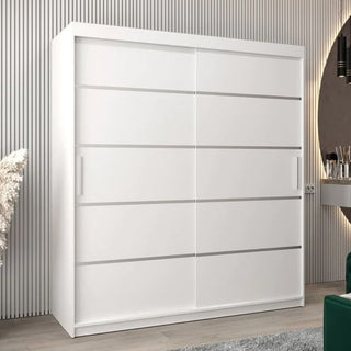 The Vevey I Wooden Wardrobe with 2 white sliding doors (180cm) and subtle horizontal grooves stands against a light, vertically-striped wall. A round mirror and small desk on the right complete the modern look.