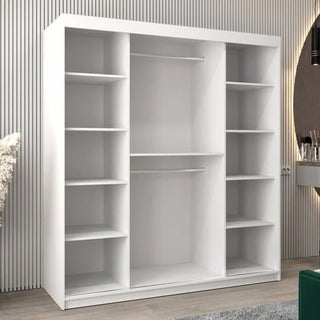 The Vevey I Wooden Wardrobe (180cm, white) features 2 sliding doors, multiple shelves on both sides, and two central hanging rods. It is shown against a vertically grooved wall in a modern room.