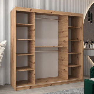 A Vevey I Wooden Wardrobe with 2 sliding doors in artisan oak (200cm) stands against a wall with vertical grooves. A vanity with a mirror and a green chair are partially visible on the right.