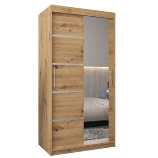 The Vevey II Mirrored Wardrobe features two sliding doors in artisan oak; one door has a wood grain finish with metal accents, while the other is a full-length mirror reflecting a bed and part of the bedroom.