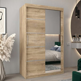 The Vevey II Mirrored Wardrobe with 2 sliding doors in Sonoma Oak (120cm) enhances a modern bedroom with gray walls, decorative plants, and a bed partially visible in the full-length mirror.