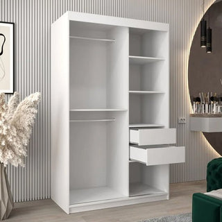 A white Vevey II Mirrored Wardrobe with 2 sliding doors (120cm), two hanging rods, multiple shelves, and two partially open drawers stands in a modern room with striped walls and decorative accents.