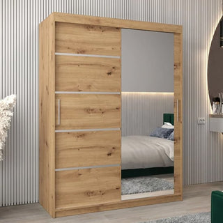 The Vevey II Mirrored Wardrobe with 2 sliding doors in artisan oak (150cm) features a sleek mirrored front and silver handles, standing against a grooved wall and reflecting the room’s modern bed and minimalist decor.