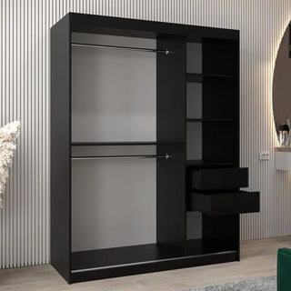 The Vevey II Mirrored Wardrobe in black (150cm) features two sliding doors, two hanging rails on the left, and five shelves—two with open drawers—on the right. It stands stylishly on a light wood floor beside a striped wall.