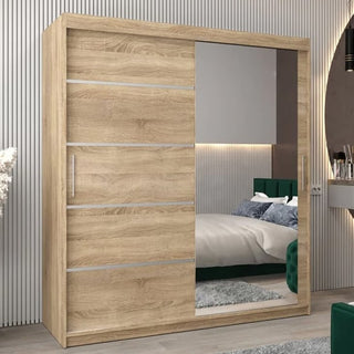 A Vevey II Mirrored Wardrobe with 2 sliding doors in Sonoma Oak, one featuring a large mirror, stands in a modern bedroom, reflecting green accents and enhancing the contemporary decor.