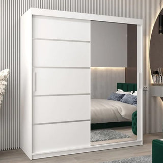 The Vevey II Mirrored Wardrobe with 2 sliding doors (180cm, white) features one solid side and one full-length mirror, reflecting a modern bedroom with a bed, green headboard, and neutral décor.