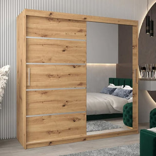 The Vevey II Mirrored Wardrobe 2 Sliding Doors 200cm in Artisan Oak features one mirrored and one oak-finished door with metal accents, perfect for a modern bedroom reflecting a green upholstered bed.