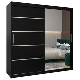 The Vevey II Mirrored Wardrobe 2 Sliding Doors 200cm in Black has one solid black door with silver lines and one mirrored door, reflecting a stylish bedroom scene with a bed, cushions, and part of the wall.