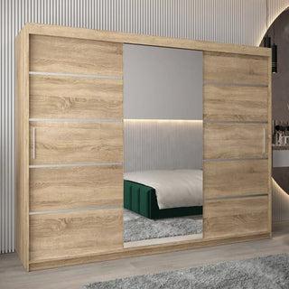 The Vevey II Mirrored Wardrobe 3 Sliding Doors 250cm in Sonoma Oak stands in a modern bedroom, its central full-length mirror reflecting the bed, gray rug, and vertical wall paneling.