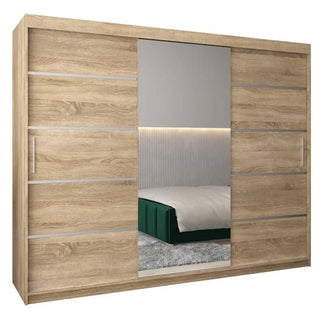 The Vevey II Mirrored Wardrobe with 3 sliding doors (250cm) in Sonoma Oak features a large central mirror that reflects a green-upholstered bed and gray carpet, complementing its natural finish.