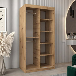 The Vevey III Mirrored Wardrobe 2 Sliding Doors 100cm in Artisan Oak has two sections: one with two hanging rods and another with five shelves. It is shown in a modern room with plants, wall art, and a round mirror.