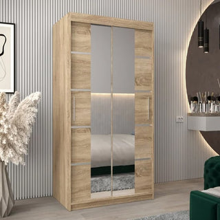 A Vevey III Mirrored Wardrobe with 2 sliding doors in Sonoma Oak (100cm) and silver handles stands in a modern bedroom, its mirrored panels reflecting the bed and wall, with decor items nearby.