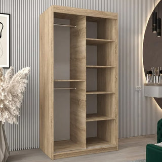 The Vevey III Mirrored Wardrobe with 2 sliding doors in Sonoma Oak stands against a vertically grooved wall, featuring shelves and two hanging rods. A green chair and pampas grass in a vase add coziness to the space.