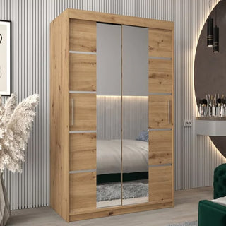 A Vevey III Mirrored Wardrobe 2 Sliding Doors 120cm in Artisan Oak stands against a striped wall, its mirrors reflecting a bed, rug, round wall mirror, and green chair, enhancing the style and spaciousness of the modern bedroom.
