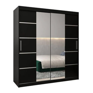 The Vevey III Mirrored Wardrobe 2 Sliding Doors 180cm in Black stands before a green-framed bed and ribbed wall panel, its mirrored doors reflecting the bedroom and part of the rug.