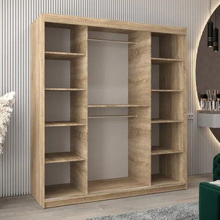 A Vevey III Mirrored Wardrobe with 2 sliding doors in Sonoma Oak stands against a vertically lined wall. To the right, a vanity table with a mirror and a green chair are partially visible.