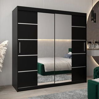 The Vevey III Mirrored Wardrobe with 2 sliding doors (200cm, black) stands in a modern bedroom with striped wall panels, a green bed, a round floating vanity, and pampas grass decor on the left.