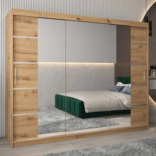 The Vevey III Mirrored Wardrobe 3 Sliding Doors 250cm in Artisan Oak stands in a modern bedroom, reflecting a green bed with white bedding and pillows, light gray walls, and a gray rug on the floor.