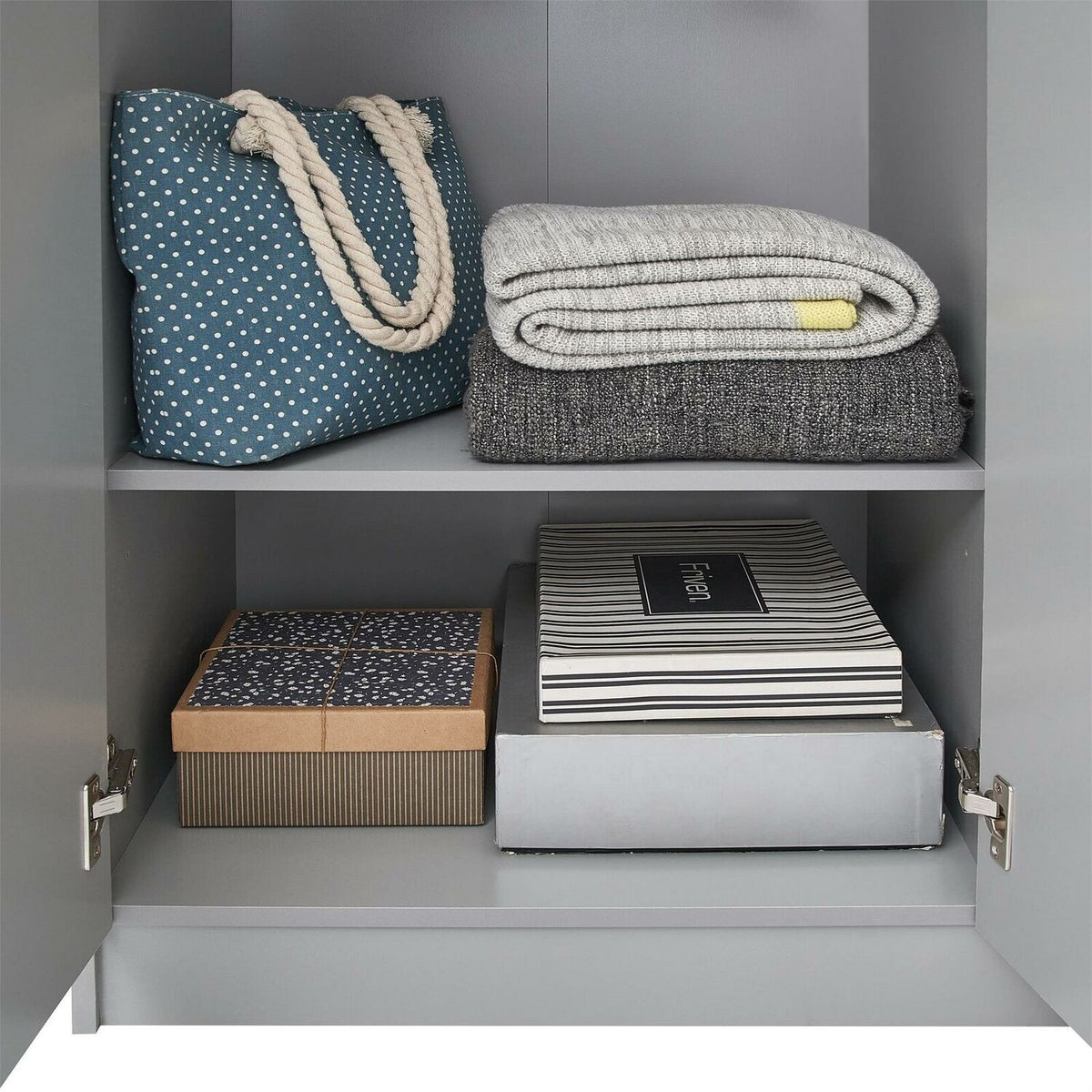 Grey wardrobe interior with blue polka dot bag on top shelf alongside folded blankets; two boxes stored on lower shelf.