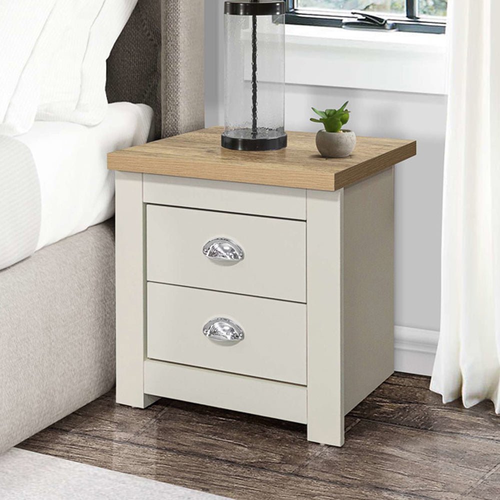Highland cream wooden bedside cabinet with 2 drawers and oak top, beside a bed.