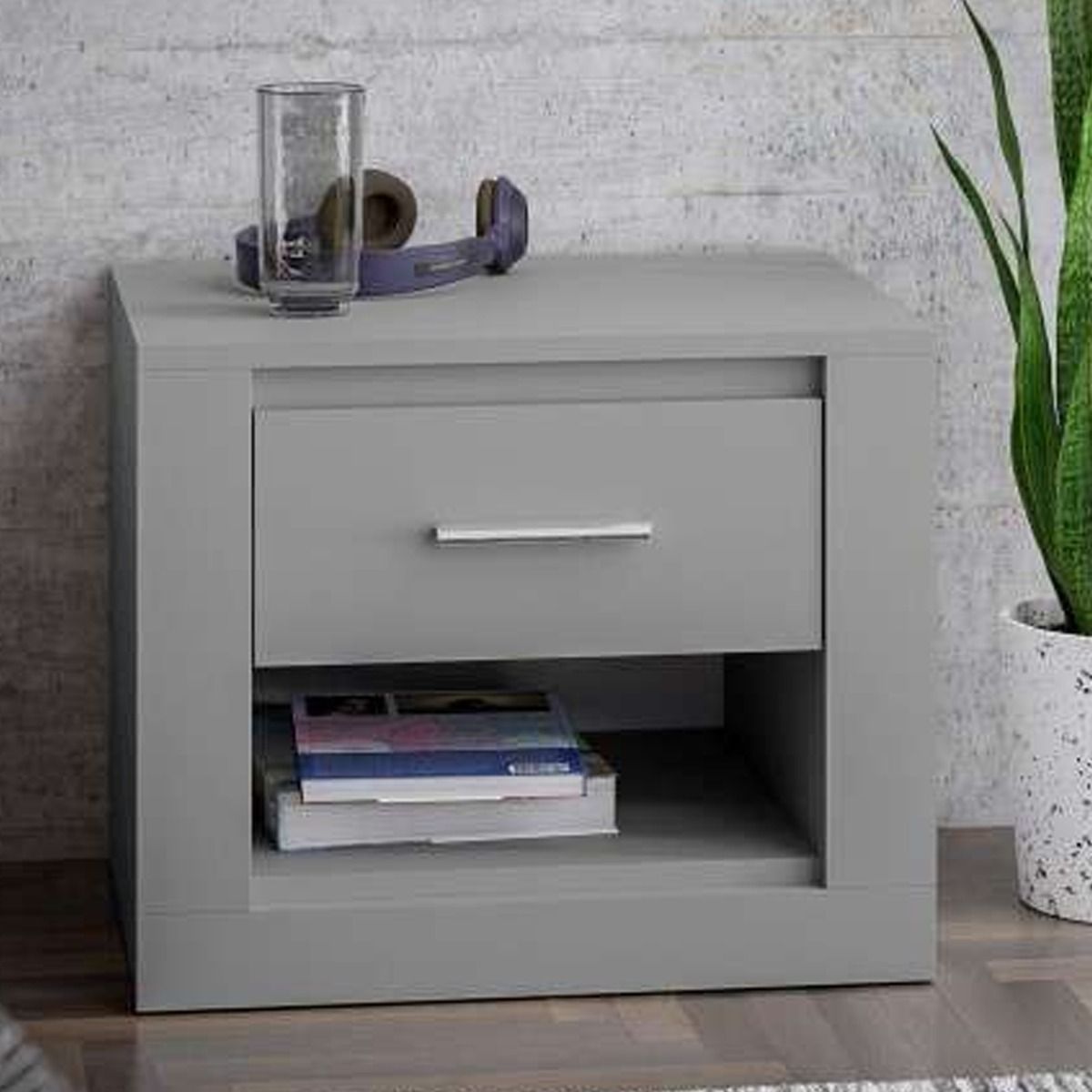 Grey bedside table with a single drawer, open shelf, and silver handle, featuring a glass and headphones on top.