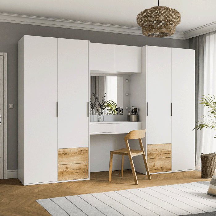 A modern bedroom showcases the BRAVYN 6 Door Mirrored Wardrobe with 6 Drawers and Dressing Table in white (300cm), complemented by a wooden chair, decorative items, woven pendant light, plant, and a light striped area rug.