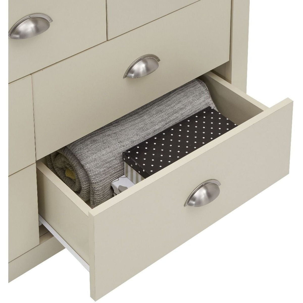 Cream chest of drawers open, showing a grey blanket and a patterned box.