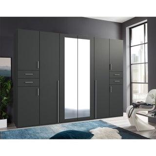 The FENTON 6 Door Mirrored Wardrobe in graphite finish (270cm) features cabinets, drawers, and a central mirror. It stands against a dark wall in a naturally lit room with a rug, plant, and chair.