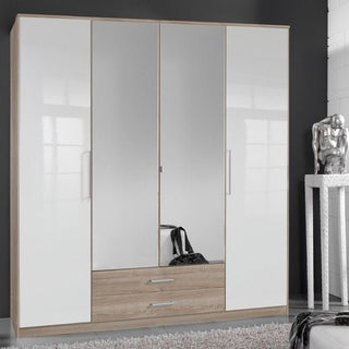 The GEMA 4 Door Mirrored Wardrobe (Oak & White Gloss, 180cm) features a wood frame, two high gloss white doors, two central mirrored doors, and two drawers underneath—a black handbag sits inside; nearby is a metallic sculpture on a table.